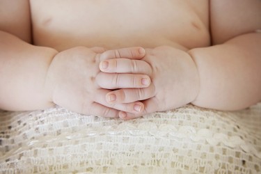 Close up of baby hands, fingers interlinked on belly