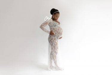 Pregnant lady looking down at her belly in her hands wearing a white flowing dress